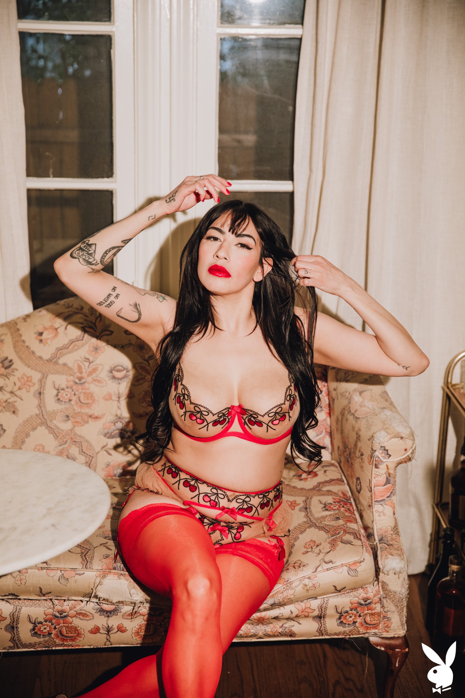 Sabina Magic Lounges In Fiery Red Lingerie On A Floral Couch In An Intimate Bedroom Setting