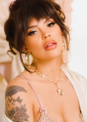 Emma Jade in lace lingerie and robe poses seductively on a plush bed with tattoos glowing